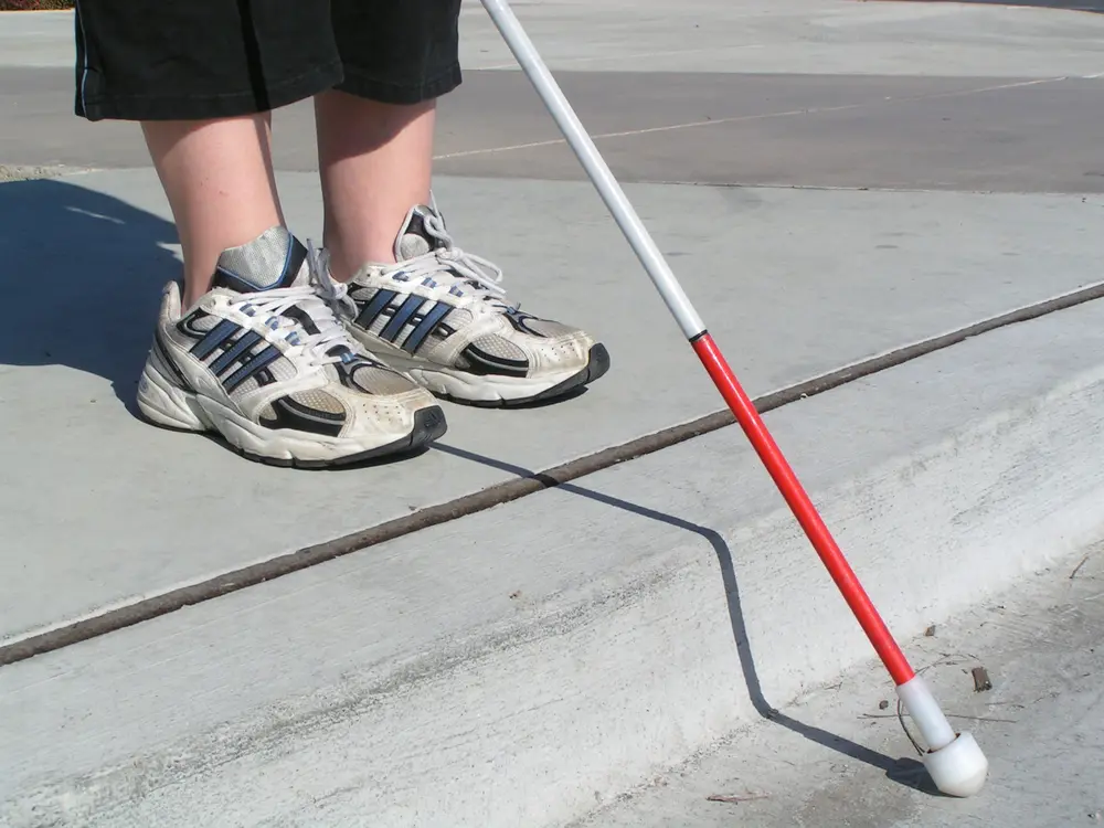 The feet of a person on the end of a sidewalk with a white cane
